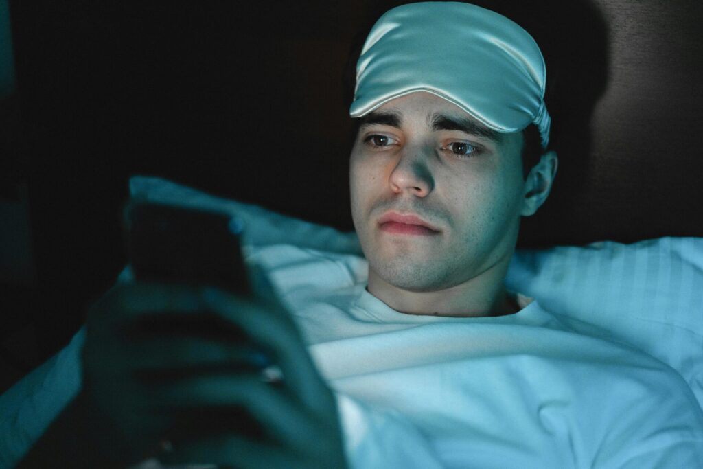 Man using phone in bed at night, an obstacle to restful sleep and one of the habits to change in steps to beat insomnia.