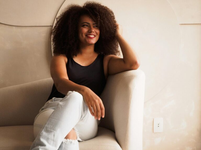 Smiling woman sitting on a couch, radiating positivity and calm—perfectly reflecting manifestation tips for beginners focused on mindset and gratitude.