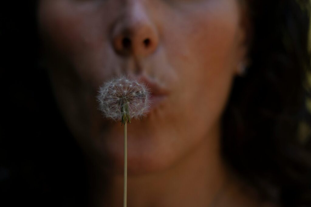 Woman blowing a dandelion, symbolizing intention setting and one of the gentle manifestation tips for beginners