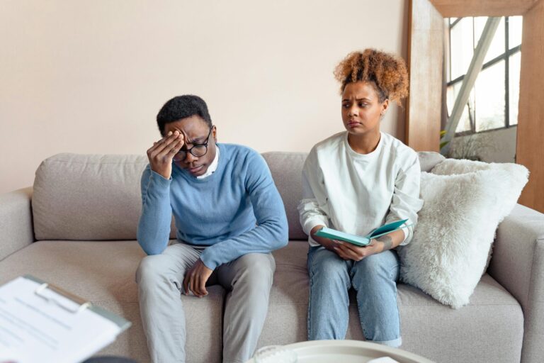 "Man holding his head while woman speaks, illustrating toxic behavior in a relationship such as emotional pressure, blame, or one-sided communication.