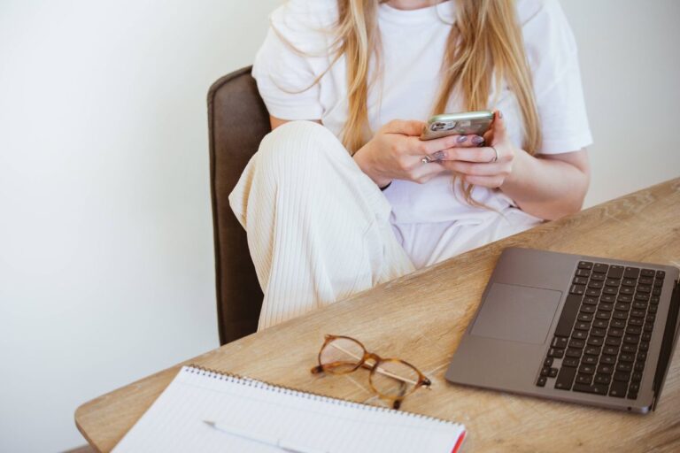 woman working on her computer at home but distracted by her phone, learning how to be productive at home