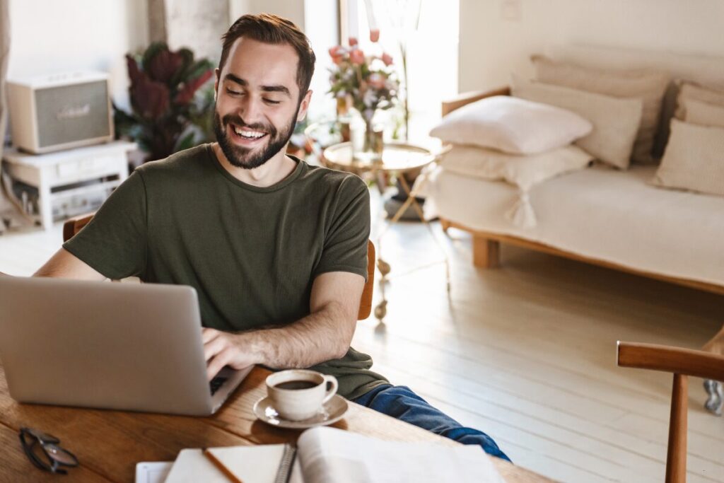 man happily working at his computer in the living room, staying productive at home