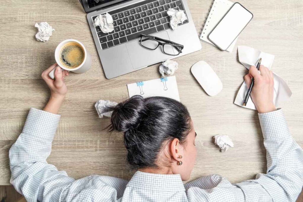 woman resting her head on a desk full of papers and coffee, overwhelmed and needing ways to reduce daily stress naturally