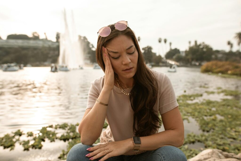 Young woman sitting outdoors, using quick anxiety relief techniques like massaging her head to calm her mind and reduce stress.