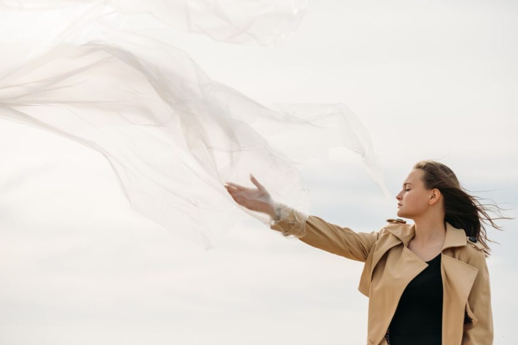 woman outdoors letting go of a scarf, eyes closed, feeling free and trusting herself instead of seeking external validation