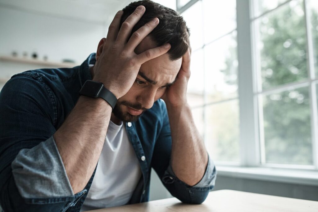 man sitting at a desk holding his head, appearing anxious and searching for natural ways to reduce anxiety