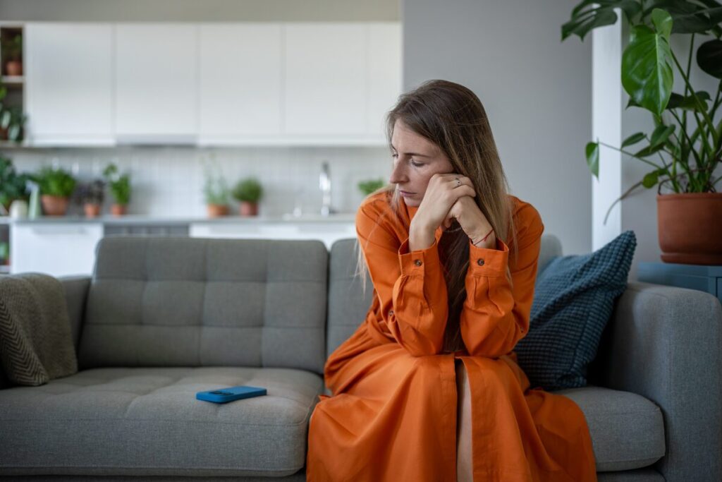 Woman sitting on a couch looking at her phone after a breakup thinking about her ex