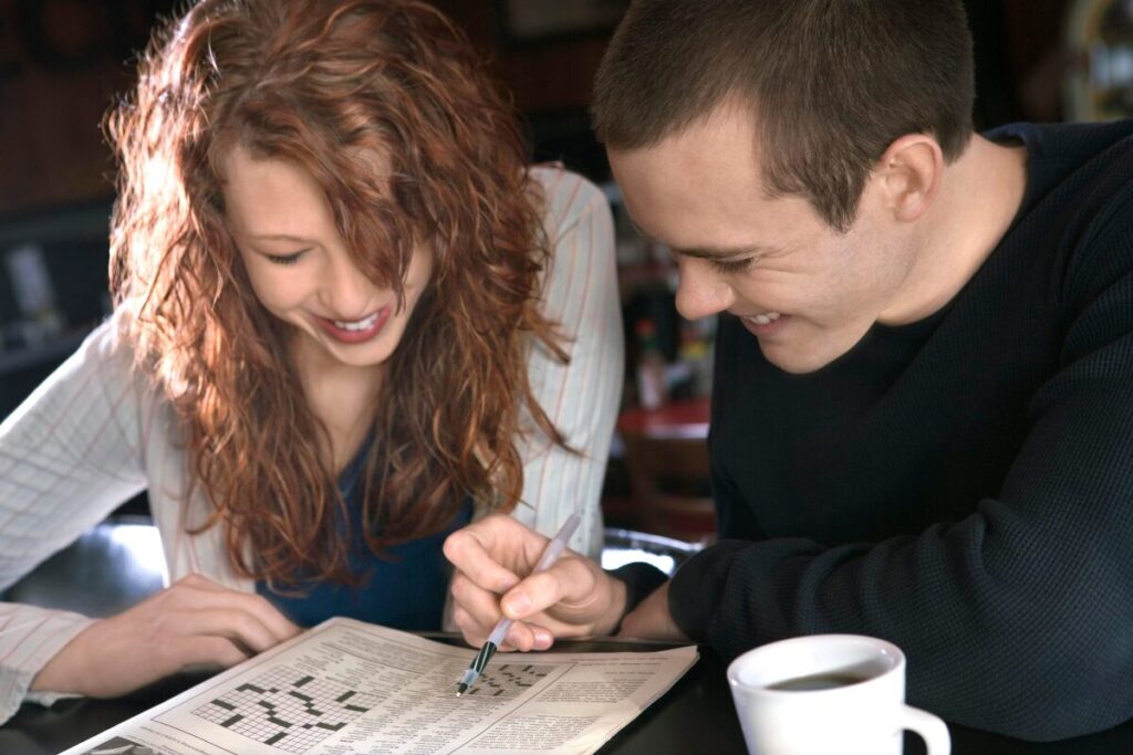 Couple solving a crossword puzzle together at home, enjoying an indoor cheap date idea.