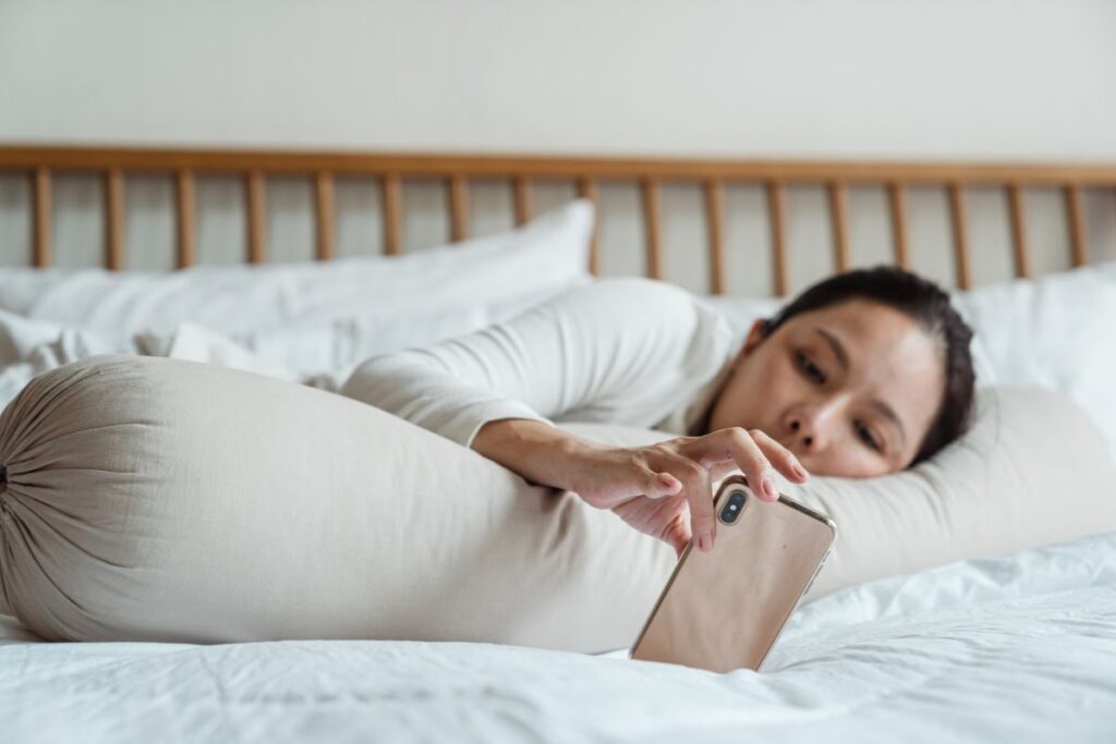 woman lying in bed scrolling on her phone, struggling with laziness and lack of motivation