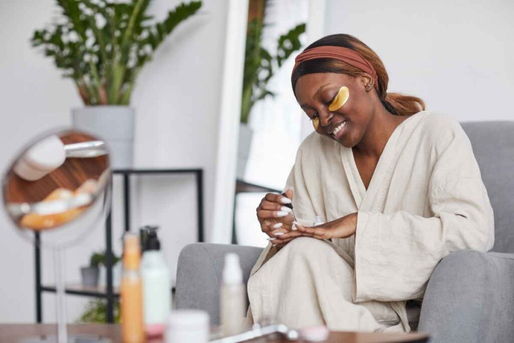 Weekend self-care idea: woman painting her nails and using under-eye pads for a relaxing self-care session at home