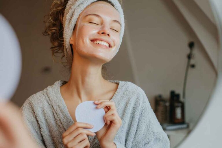 Weekend self-care idea: woman removing makeup and smiling, enjoying a relaxing evening at home