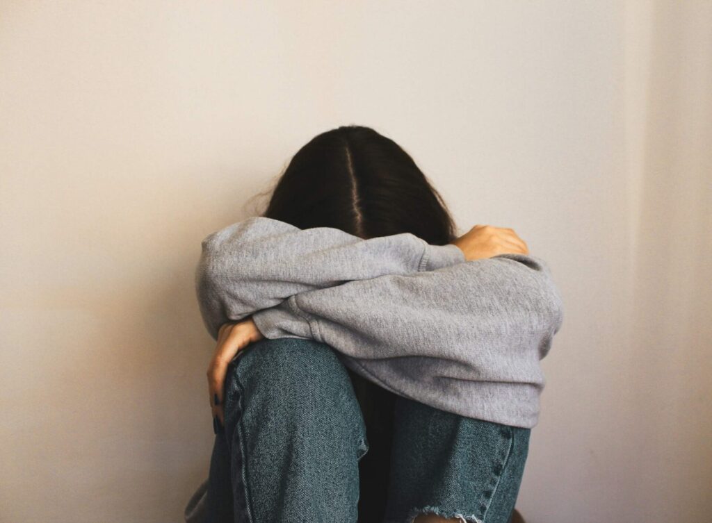 Girl sitting on the floor covering her face with her hands, illustrating coping with loneliness when you have no one to turn to.