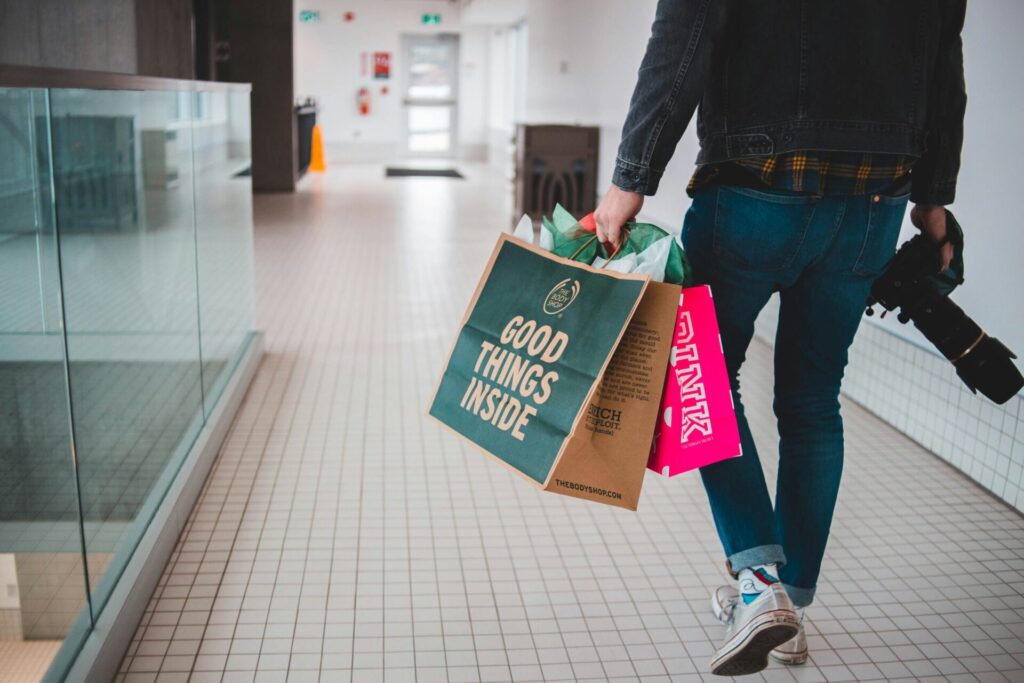 Man carrying shopping bags while walking through a store, illustrating everyday challenges related to how to stop being a materialistic person.

