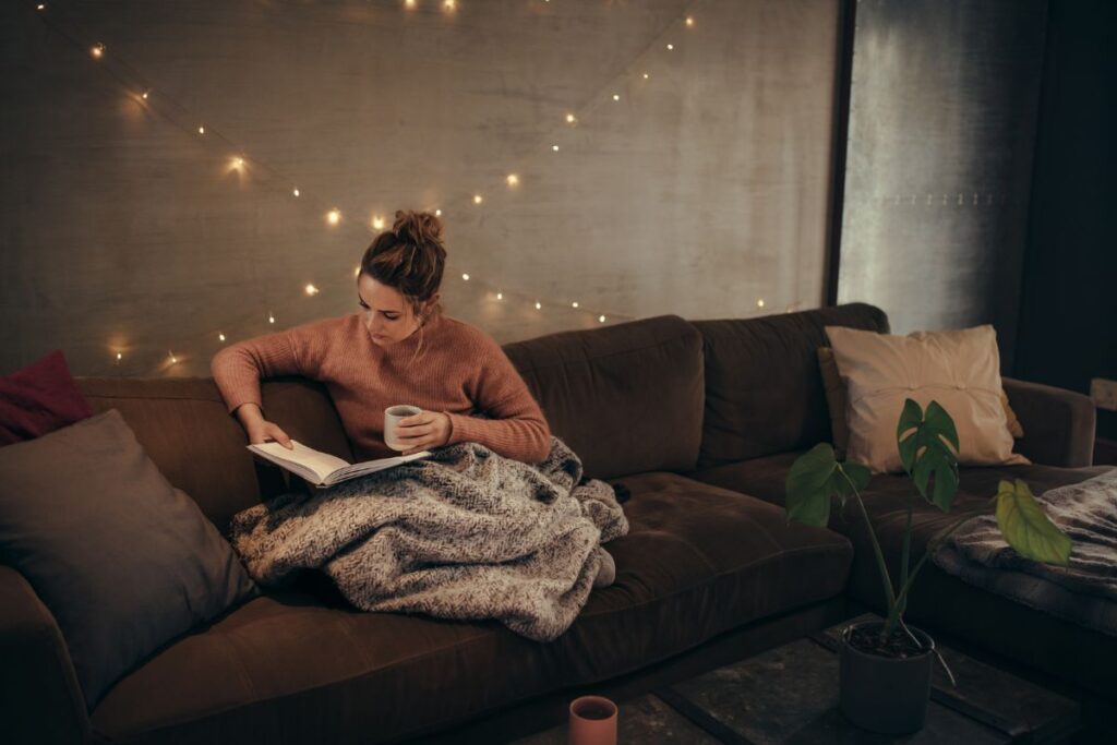 Ways to combat holiday stress: woman sitting on a sofa in a Christmas-decorated room, reading a book and relaxing during the holidays