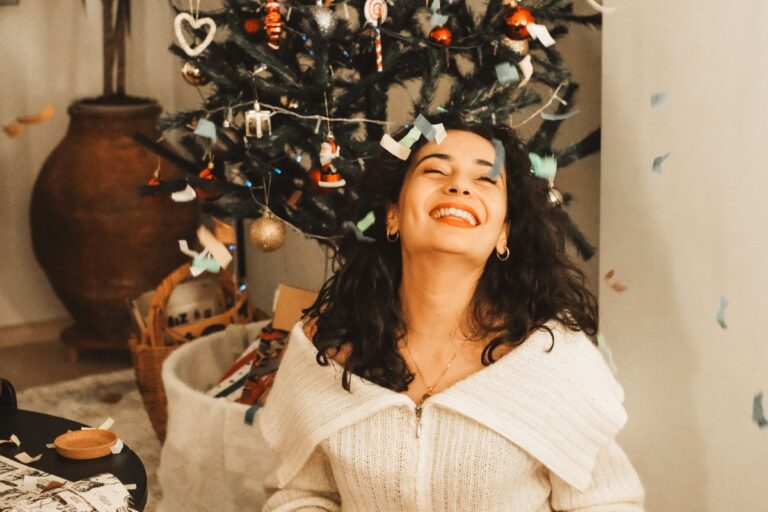 Ways to combat holiday stress: woman sitting happily under a Christmas tree, embracing calm and joy during the holiday season