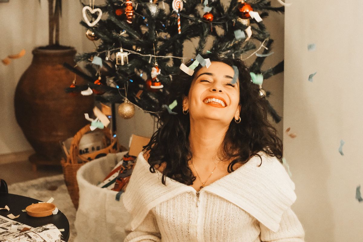 Ways to combat holiday stress: woman sitting happily under a Christmas tree, embracing calm and joy during the holiday season