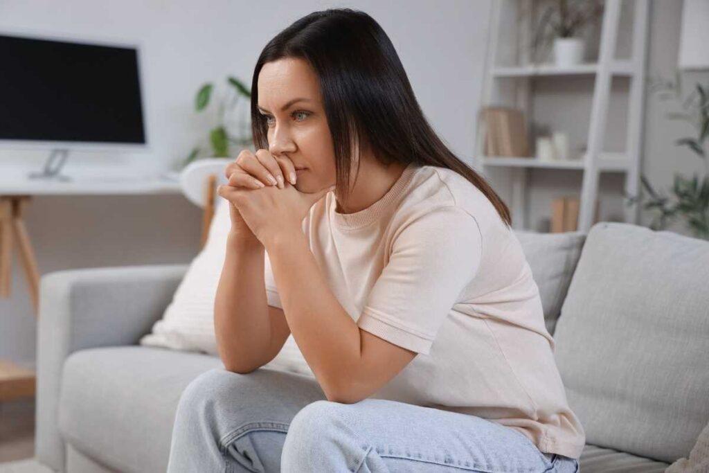 Natural ways to calm stress at home: woman sitting on the sofa, thinking and reflecting to manage stress naturally
