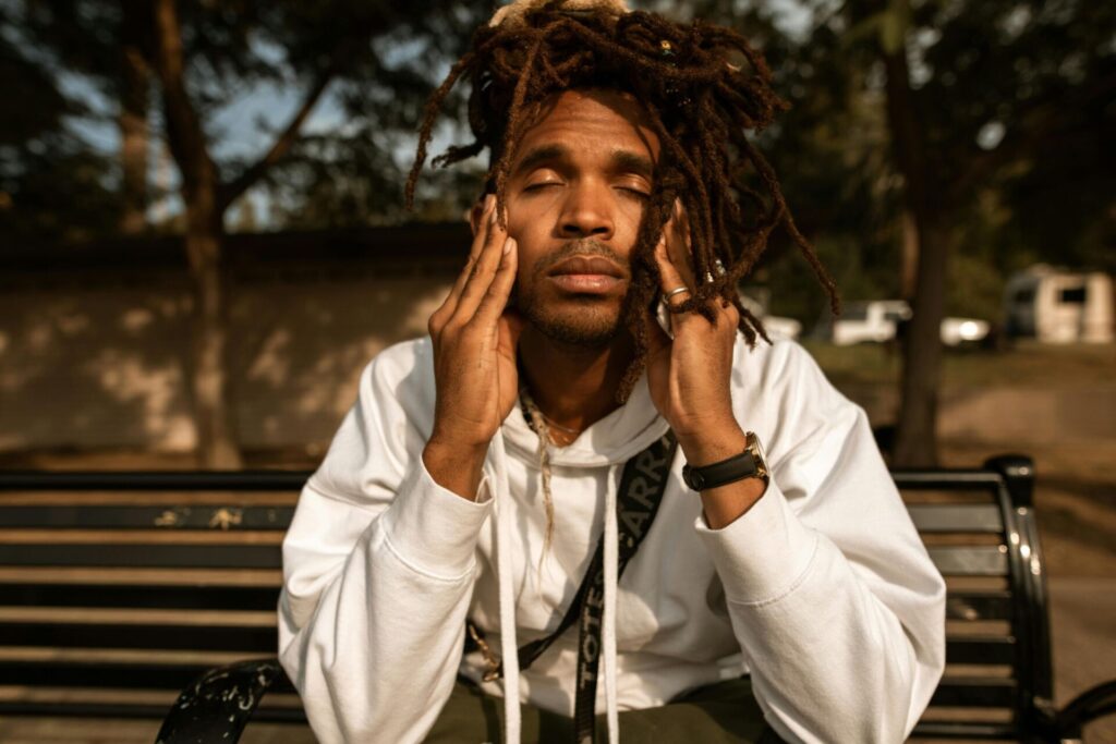 Dark-skinned man sitting outdoors with closed eyes, deep in thought — showing inner reflection often triggered by honest questions to recognize childhood trauma.