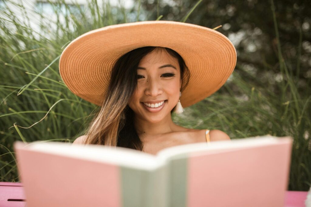 Smiling woman in a hat holding a book, enjoying one of her favorite books about money mindset.