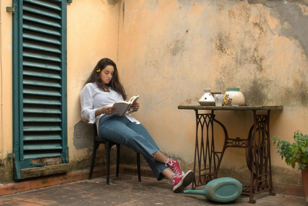 Woman relaxing on a balcony with her legs stretched out, reading books about money mindset for personal growth.