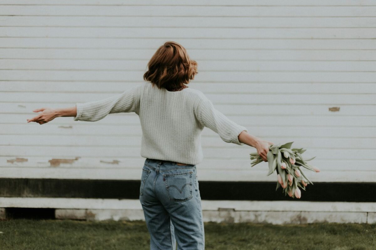A woman spinning joyfully outdoors with a bouquet in hand — a beautiful moment that reflects subtle signs you truly love yourself.