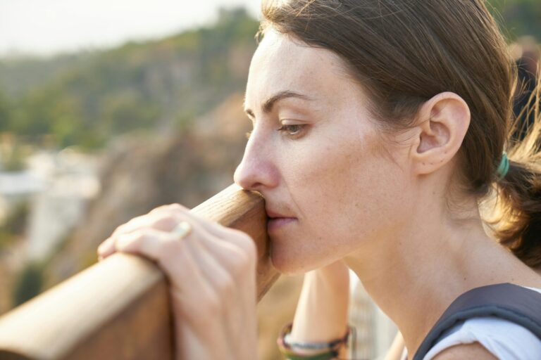 Sad woman leaning on a railing, staring into the distance while thinking about journal prompts for sadness to ease her emotions.