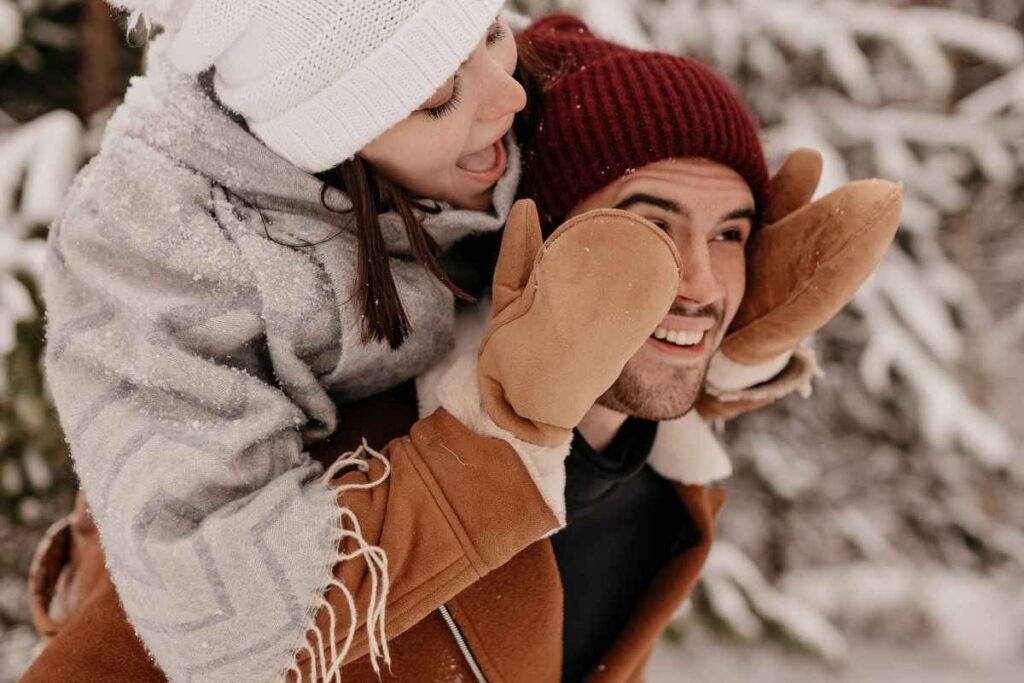 Winter bucket list ideas for adults: couple outdoors in the snow, smiling and enjoying a fun winter day together