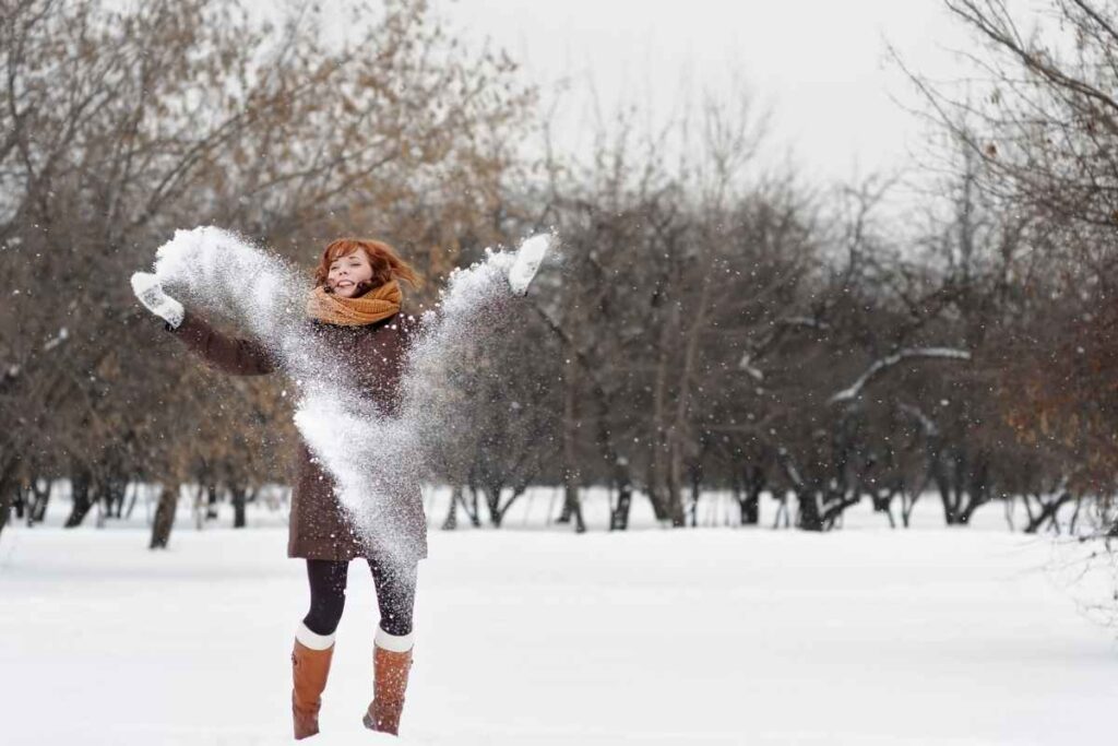 Winter bucket list ideas for adults: woman joyfully throwing snow in the air, embracing the magic of the winter season