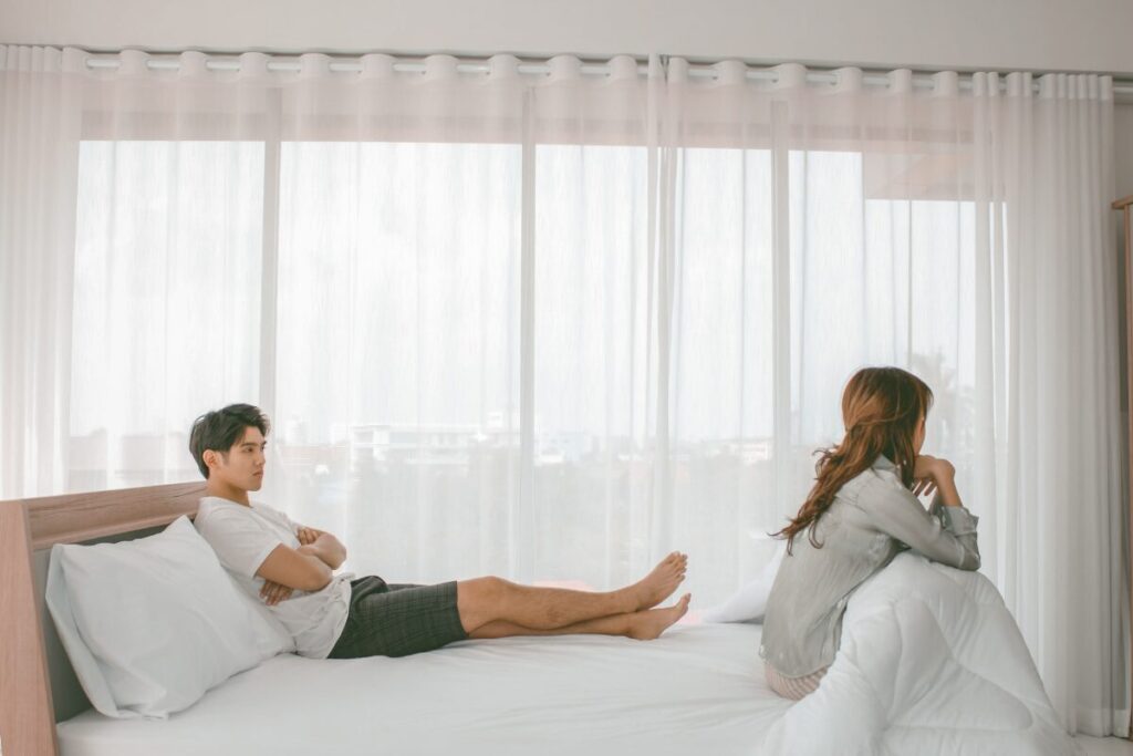 Couple sitting apart in bed showing emotional distance and signs of being taken for granted