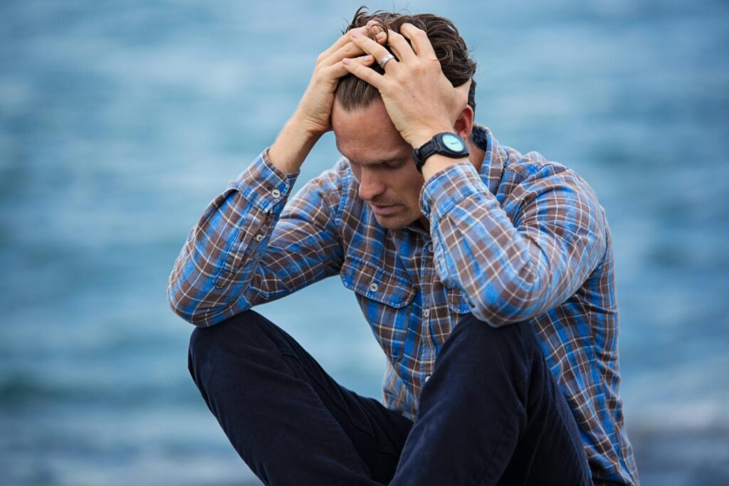Stressed man sitting outdoors with head in hands—illustrating emotional overwhelm and the importance of techniques for effective emotion regulation.