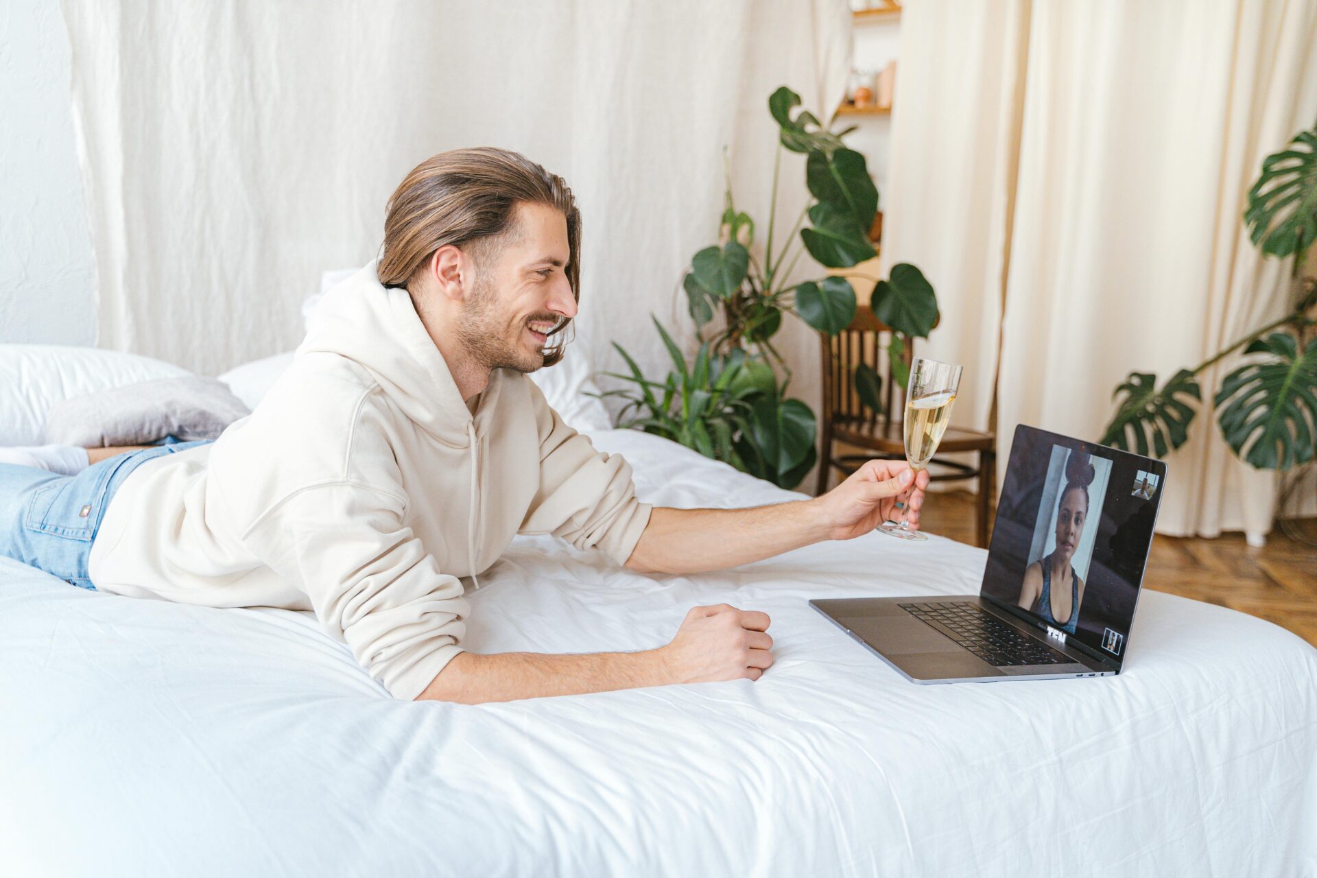 Man lying on bed video chatting with his girlfriend, both toasting over distance—highlighting emotional disconnection and what kills long-distance relationships.
