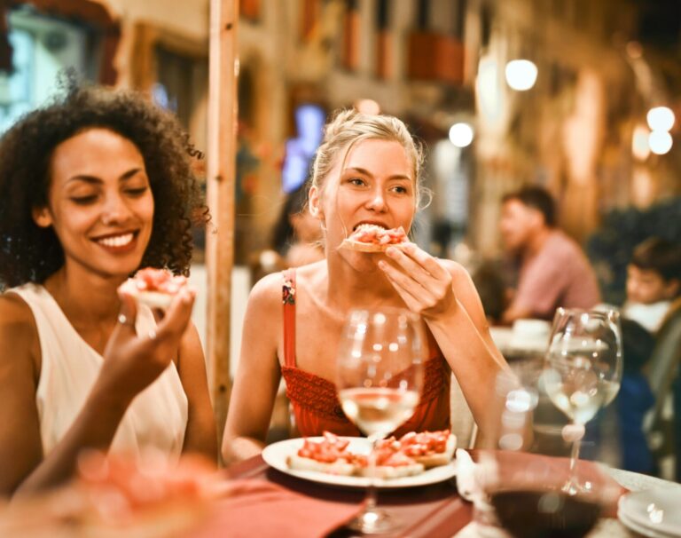 "Woman socializing with friends at a restaurant, possibly overthinking her words—capturing the internal question: Why do I apologize so much?