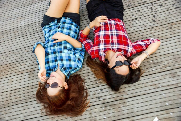 Two friends laughing together on a wooden deck, showcasing the joy and trust that are essential for how to be a good friend.