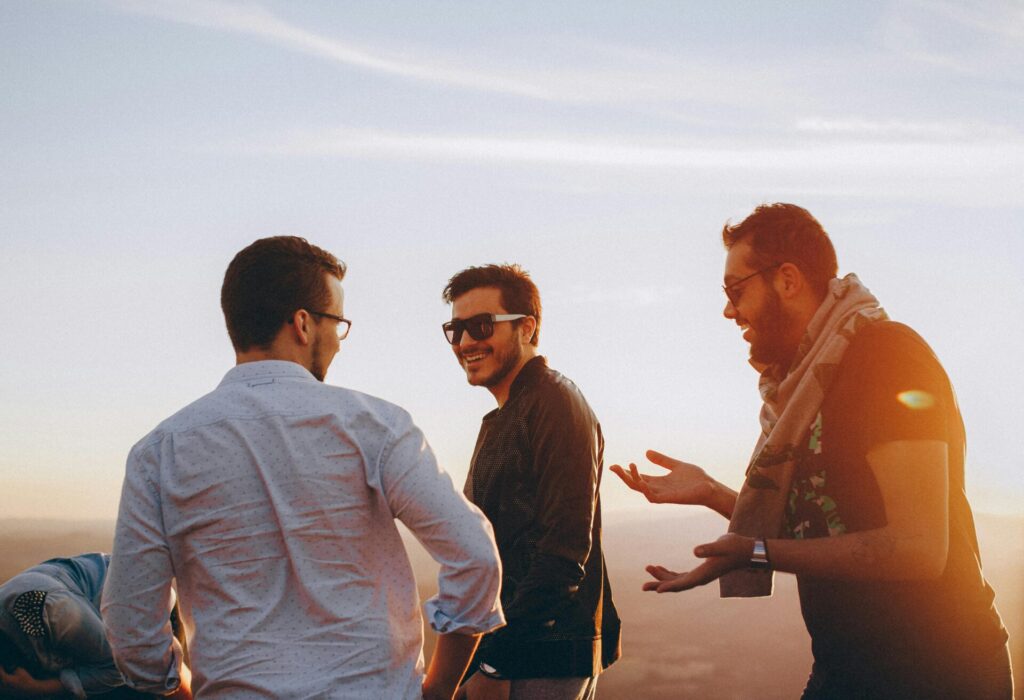 Two guys chatting and laughing in nature, embodying how to be a good friend through open communication and shared laughter.