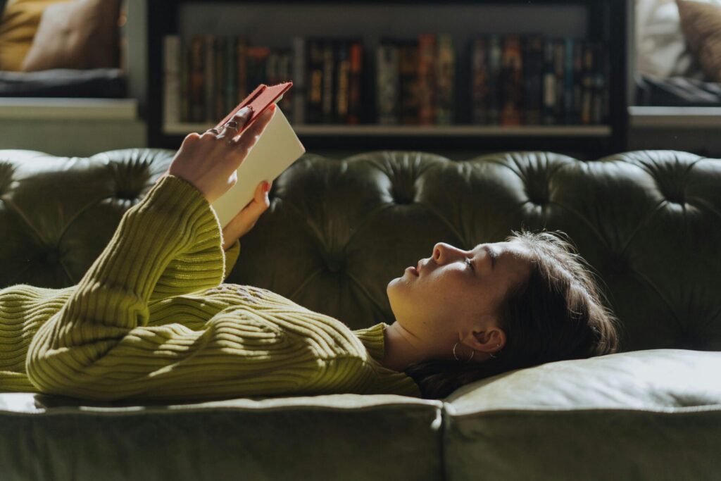 Woman lying on a couch, staring at the ceiling and holding a book, finding comfort and a way to deal with loneliness after a breakup