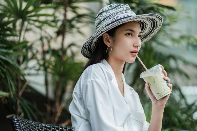 Woman wearing a hat, sitting alone outside and sipping a drink through a straw, thinking about how to improve yourself after a breakup