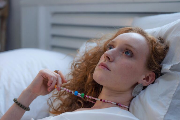 "Woman lying on bed, lost in thought and holding her necklace—capturing the feeling of overthinking and the need to learn how to stop overthinking after a first date.