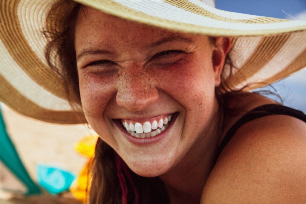 Woman wearing a sun hat at the beach, laughing joyfully, inspired by uplifting inspirational quotes for a bad day.