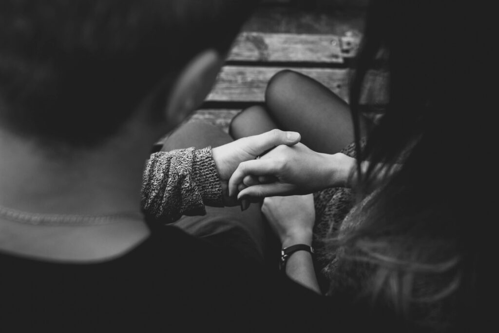 Black and white photo of a couple holding hands, subtly showing signs of fear of commitment in relationships through hesitation and emotional distance.