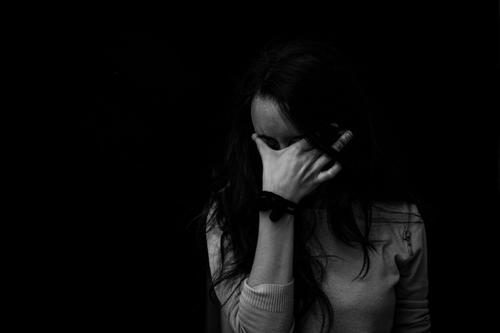 Black and white image of a woman holding her forehead with one hand, overwhelmed—depicting habits that make anxiety worse.

