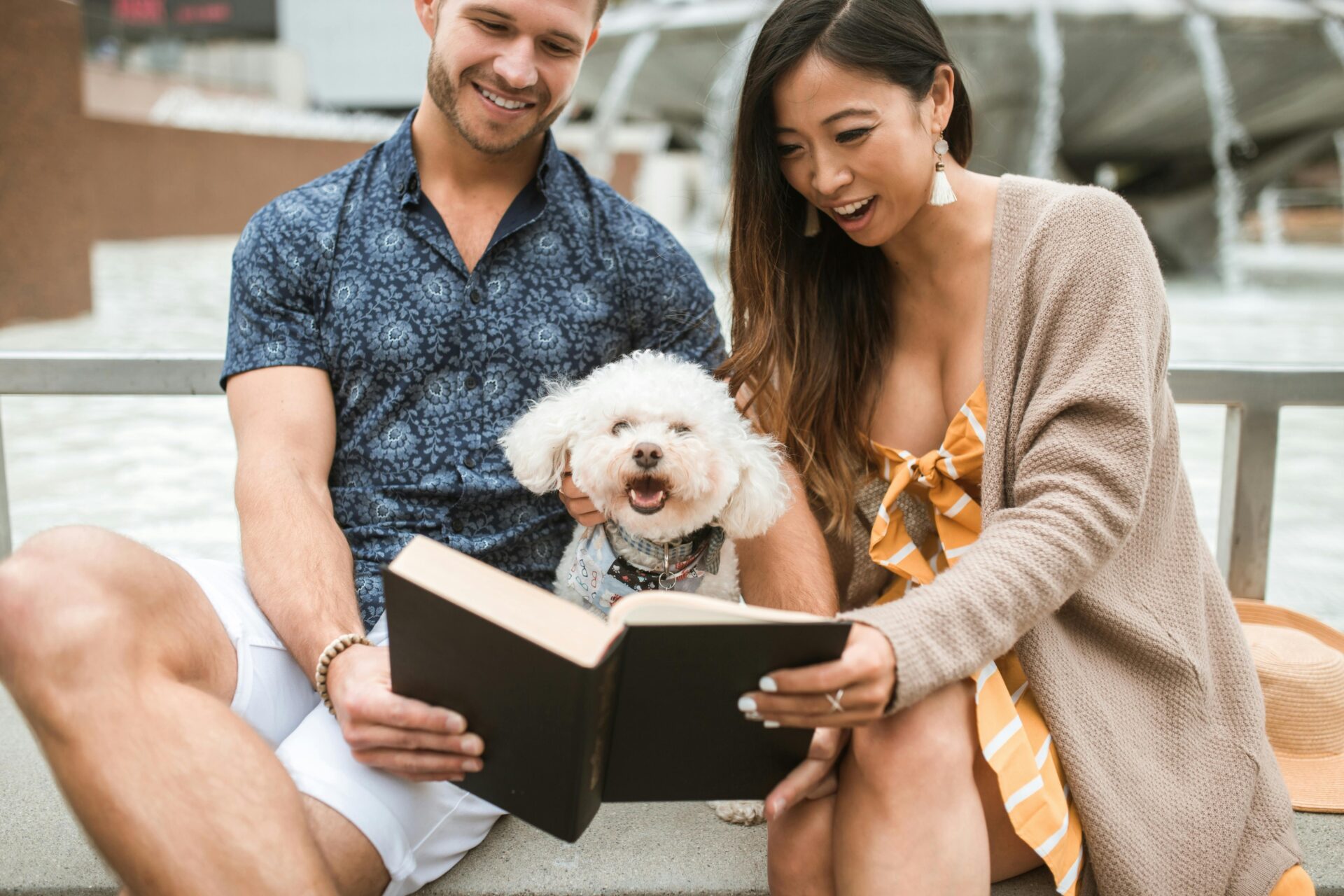 Young couple sitting outside with a white dog, smiling while reading together — enjoying one of the best marriage books for couples.