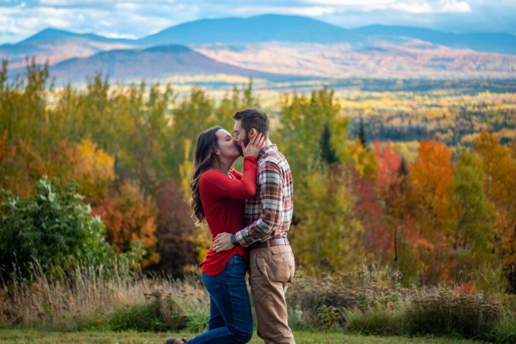 Couple kissing in nature with colorful autumn trees in the background — a romantic scene perfect for fall date ideas for couples who love the outdoors.