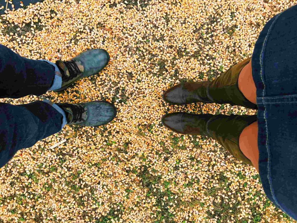 Couple standing face to face on autumn leaves, photo shows their shoes from above — a sweet and simple example of fall date ideas for couples.

