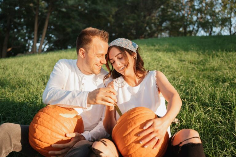 Man and woman sitting on the ground carving pumpkins and laughing — a cozy moment that captures fun fall date ideas for couples.