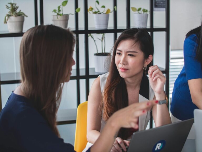 Two women sitting in an office, one speaking while the other listens attentively — a real-life moment showing how to assert yourself when you're afraid of conflict.