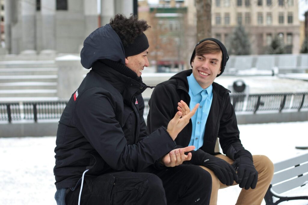 Two men dressed warmly, sitting on a snowy bench and talking openly — a simple yet powerful scene showing how to assert yourself when you're afraid of conflict in everyday life.