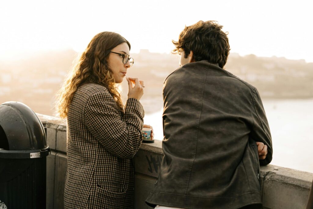 A man and woman having a calm conversation on a bridge by the river, sharing ice cream — reflecting a peaceful approach to how to assert yourself when you're afraid of conflict.