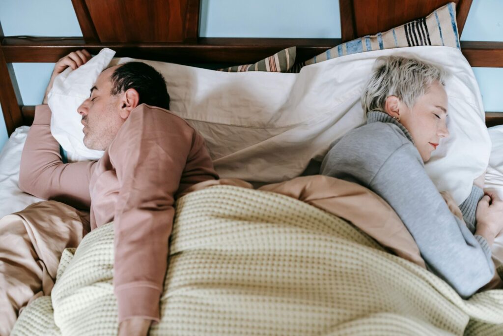 Middle-aged married couple sleeping back to back, illustrating the emotional distance when dealing with how to overcome resentment in marriage.