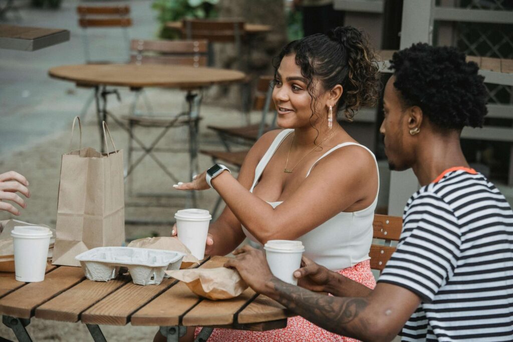 Man and woman sitting outside with drinks, woman talking passionately while man listens quietly, showing moments that teach how to stop being controlling in relationship.

