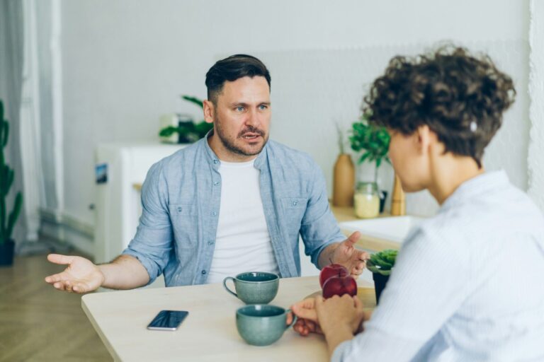 Man and woman sitting at a table, the man upset, illustrating how to stop taking everything personally in your relationship.